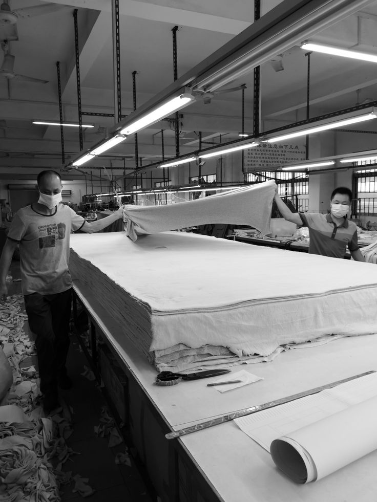 Two workers handling large sheets of fabric in a gigavibe factory setting.