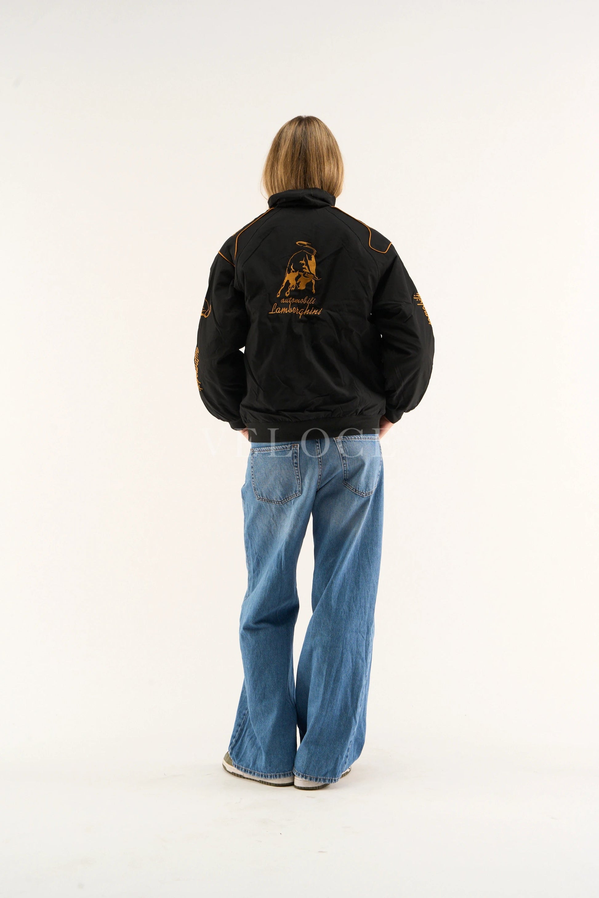 Women wearing a Lamborghini embroidered jacket women’s luxury streetwear look with a logo on the back, standing against a white background