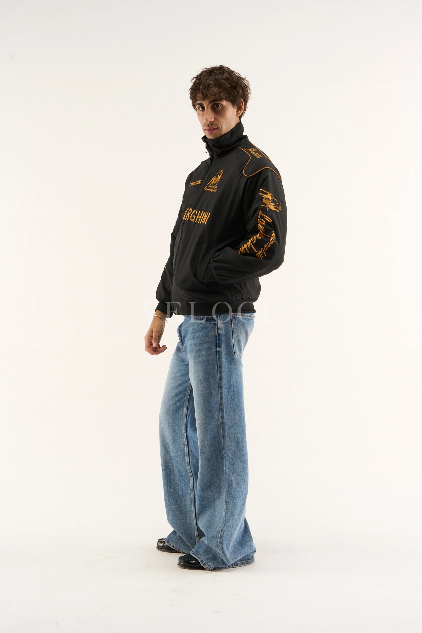 Model wearing Lamborghini embroidered jacket streetwear style and blue jeans on a white background