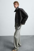 Man wearing a black leather jacket and light gray jeans against a white background