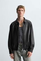 Man wearing a leather effect bomber jacket front view in black faux leather over a gray shirt on a light gray background