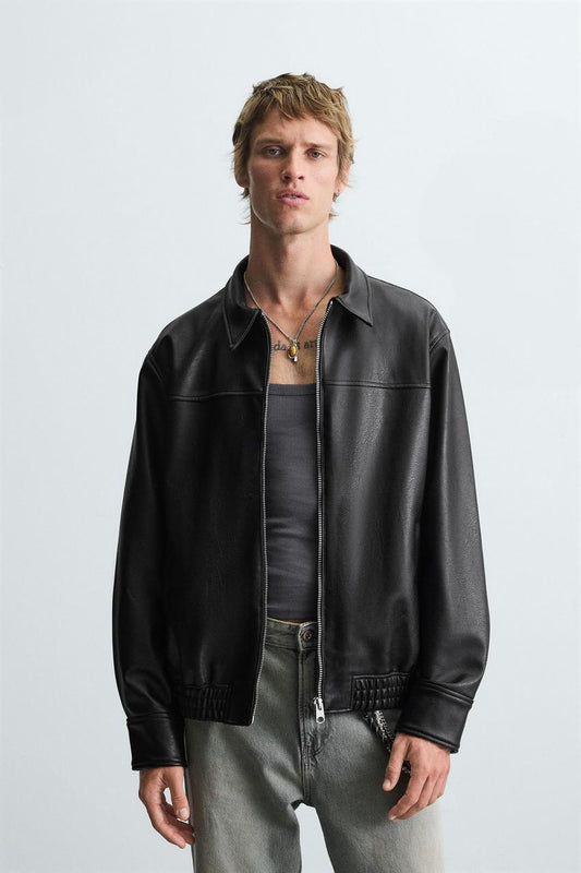 Man wearing a leather effect bomber jacket front view in black faux leather over a gray shirt on a light gray background