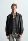 Man wearing a leather effect bomber jacket front view in black faux leather over a gray shirt on a light gray background