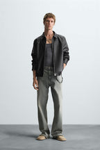 Man wearing a Gigavibe vegan leather bomber jacket in India, gray shirt, and jeans on a plain background