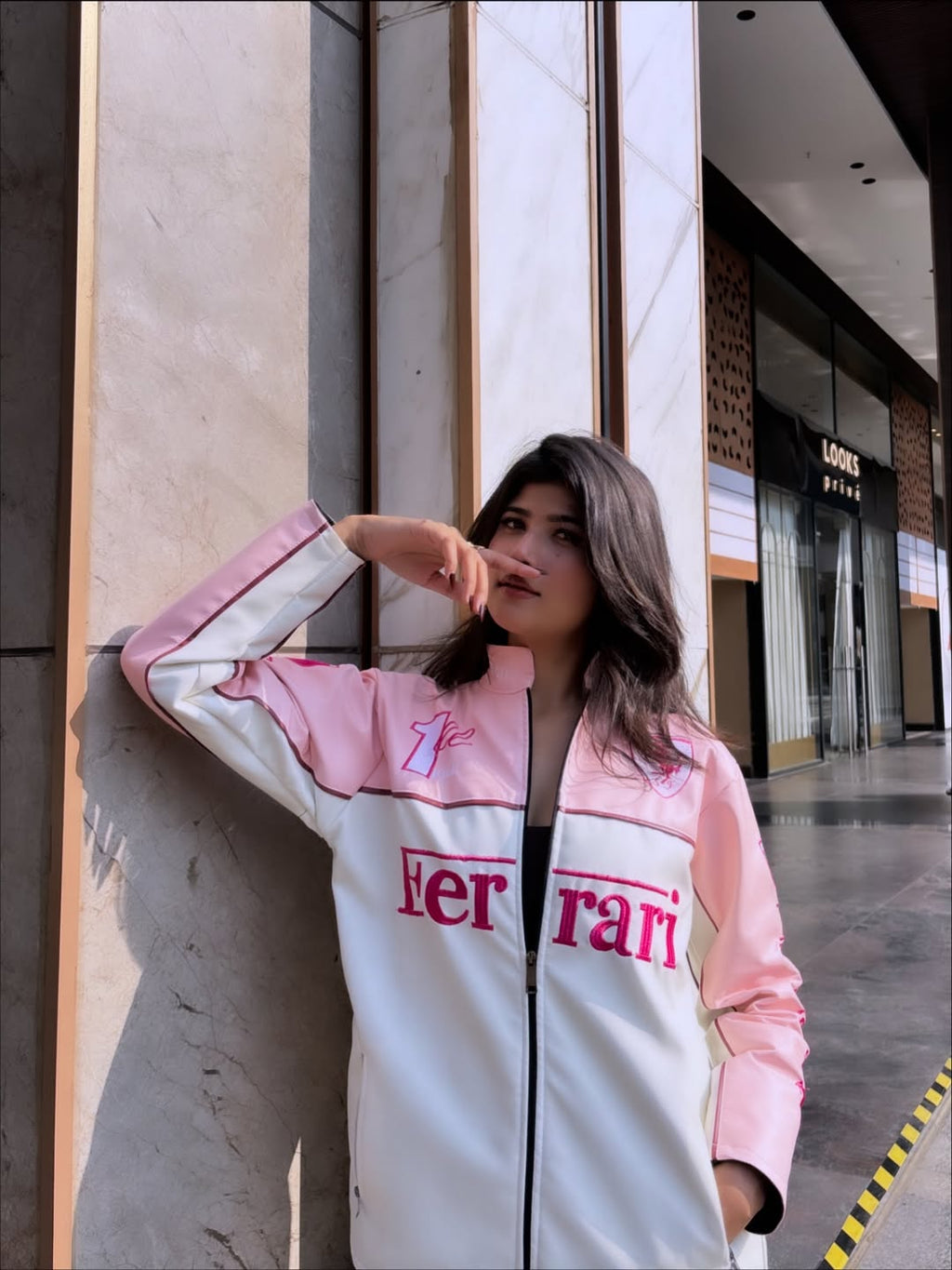 women wearing a Pink Ferrari jacket streetwear look by Gigavibe, standing against a building.