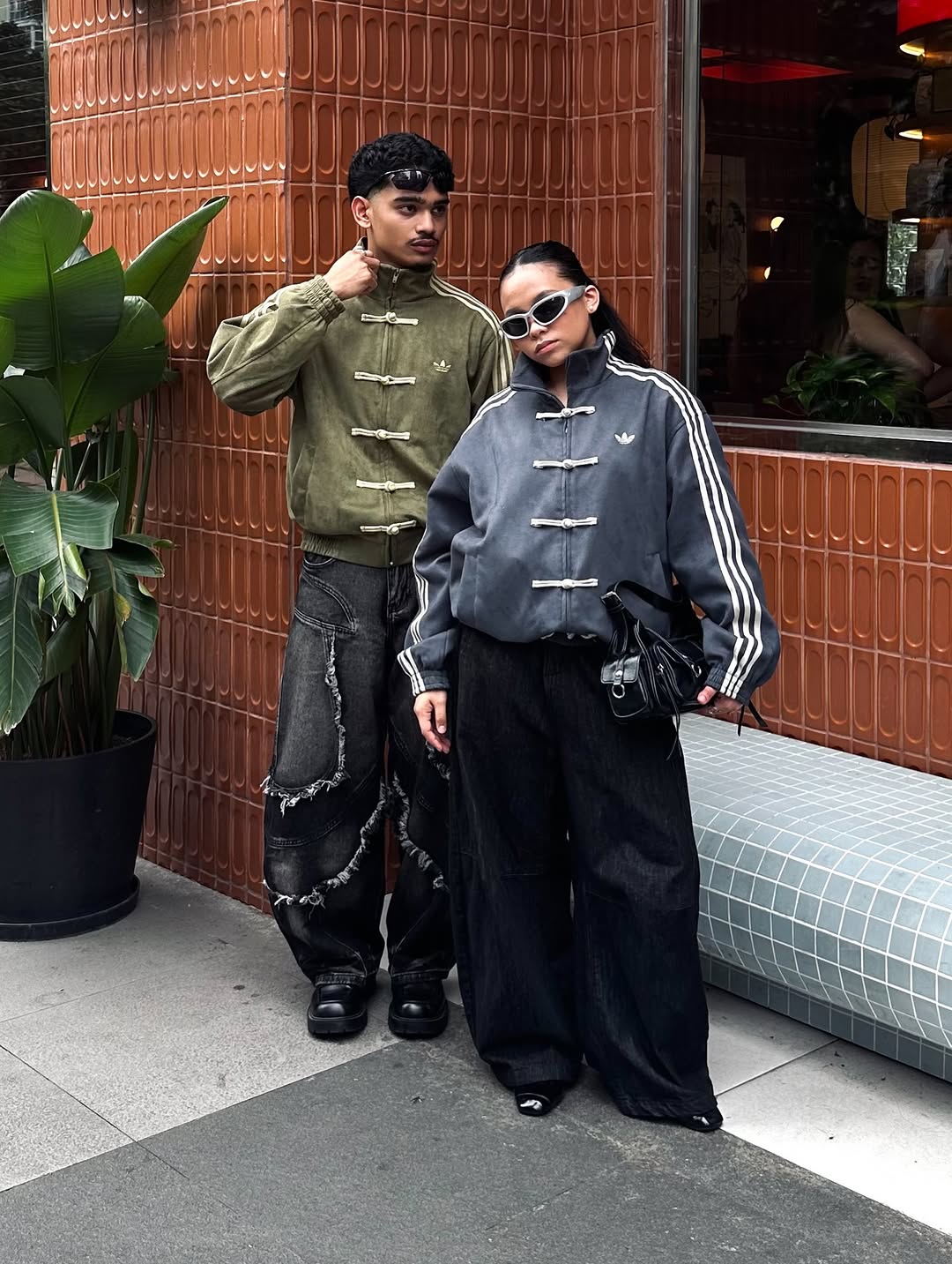 Urban city setting with the male and female models styling the massive Olive Green and Dark Grey bombers. Displays the perfect hybrid of high fashion runway draping and raw Gen Z streetwear utility.