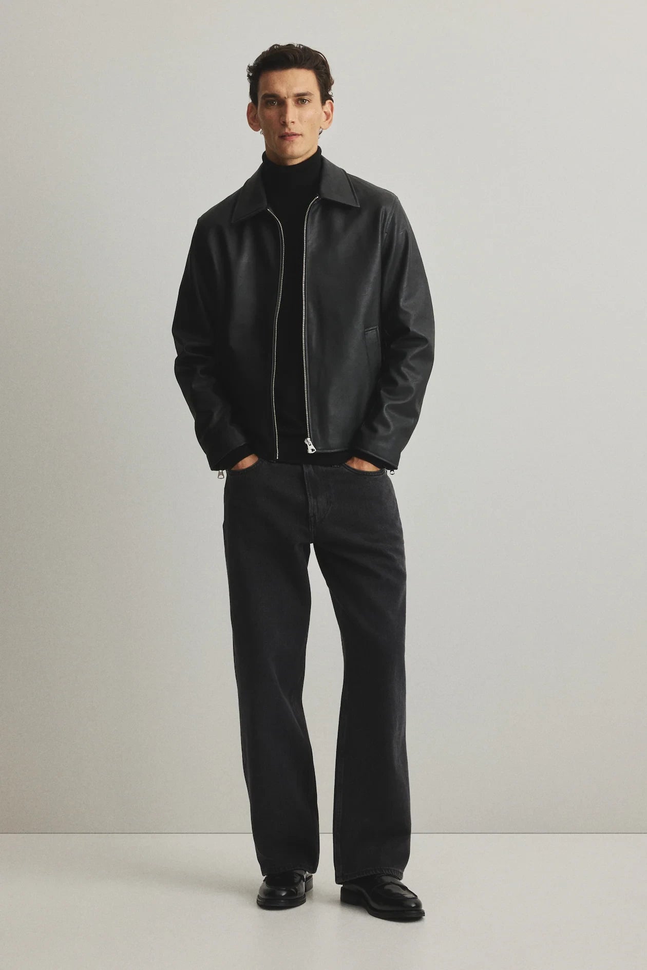 Lifestyle modeling shot displaying the unisex box cut leather jacket in an urban environment. Strongly highlights the wide structured shoulders, clean pointed collar, and the total absence of loud branding for a truly corecore aesthetic black jacket.