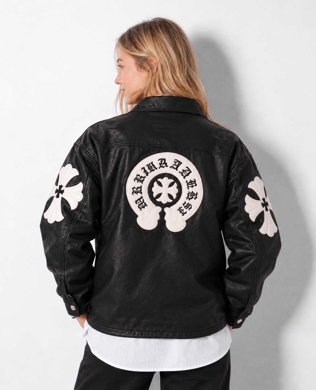 Back perspective of a female model wearing the black Gothic cross leather jacket, highlighting the rear horseshoe crest and arm patch detailing