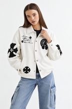 Full lifestyle street shot of a girl wearing the cream cross patch leather jacket paired with camouflage cargo pants
