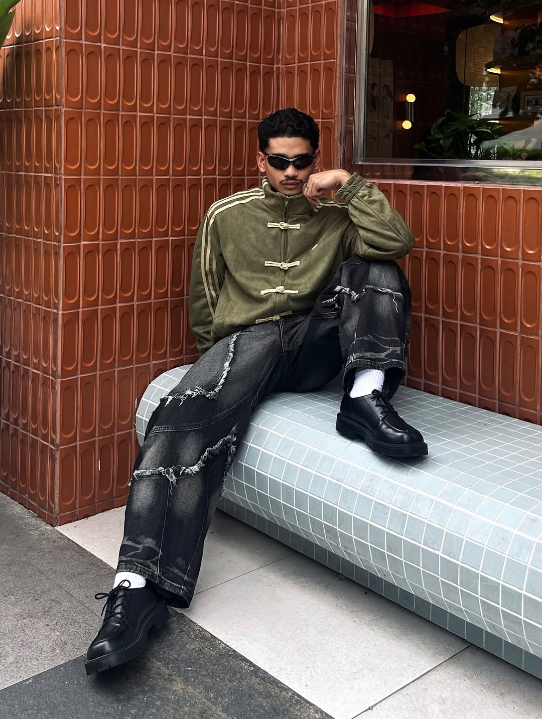 Full body outfit styling showing the male model utilizing the Olive Green Suede Bomber perfectly. Anchored with massive baggy cargo pants to emphasize the aggressive horizontal Gen-Z frame.