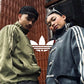 Male and female models posing in matching oversized vegan suede knot jackets in Olive and Grey. Showcasing the flawless unisex aesthetic and high-end matching streetwear couples outfit at Gigavibe.
