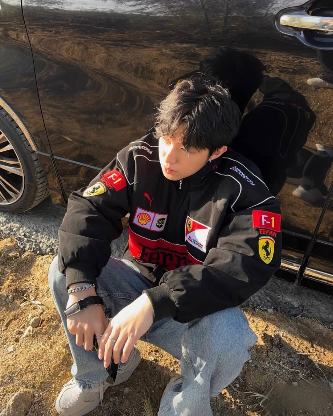 Male model wearing the unisex embroidered black Ferrari racing jacket, showcasing the structured drop-shoulder drape and vibrant chest patches