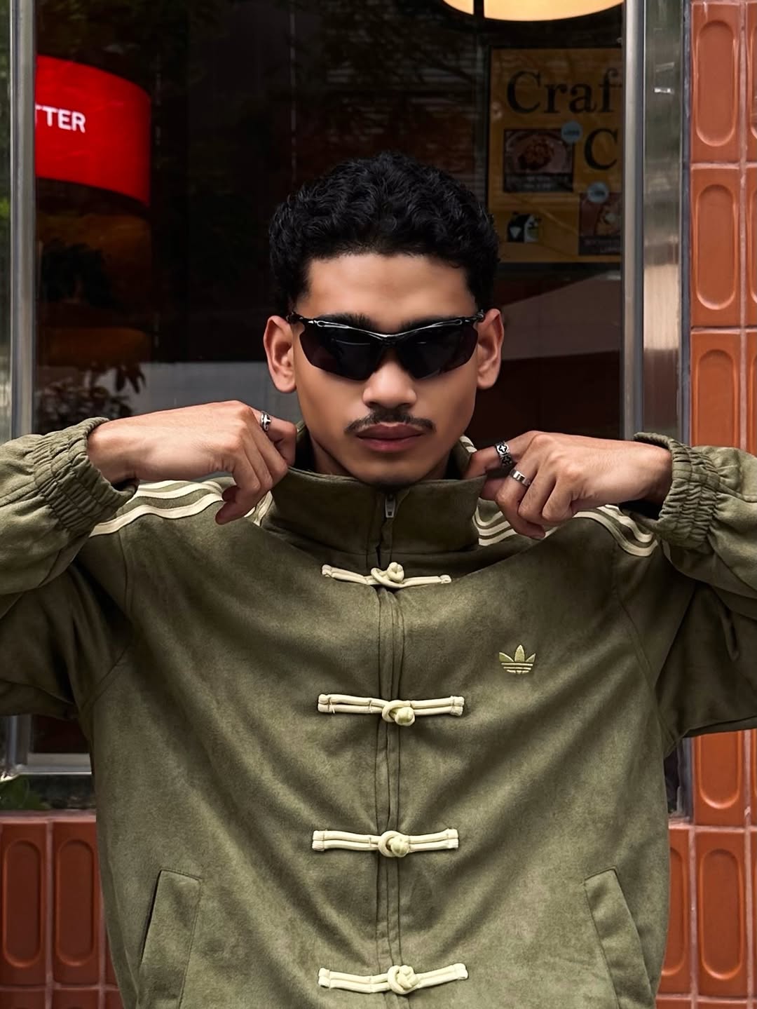 Side profile of the male model executing the box-cut aesthetic in the Olive Green Custom Knot bomber. Clearly shows the heavy 3-stripe sleeve embroidery utilized in premium vintage racing outerwear.