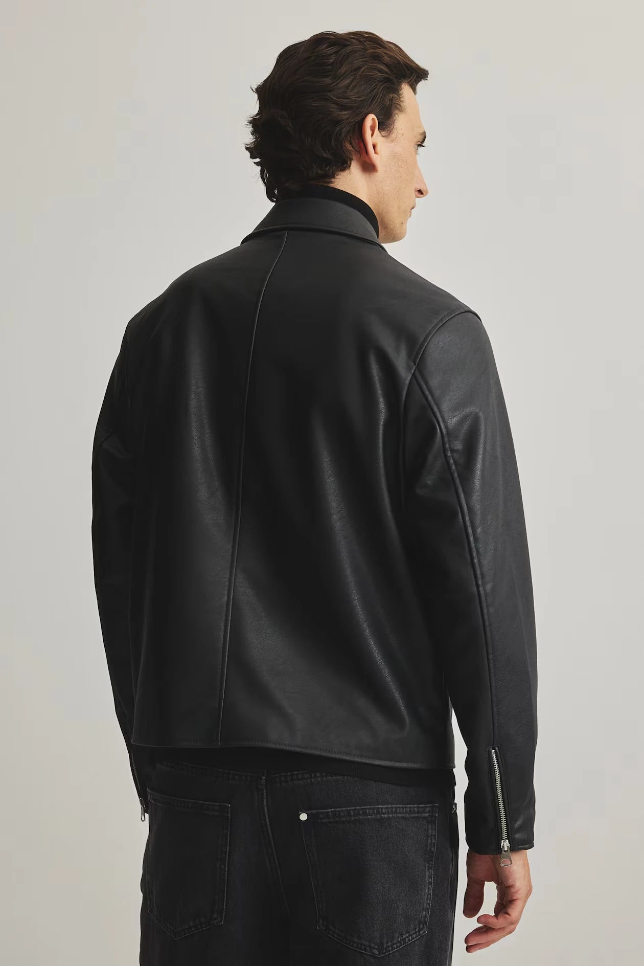 Side and profile view of the minimalist black leather box-cut jacket. Showcases precisely where the extreme dropped shoulder seam rests to emphasize the oversized streetwear architecture, ensuring a perfect gender-neutral darkwear silhouette.