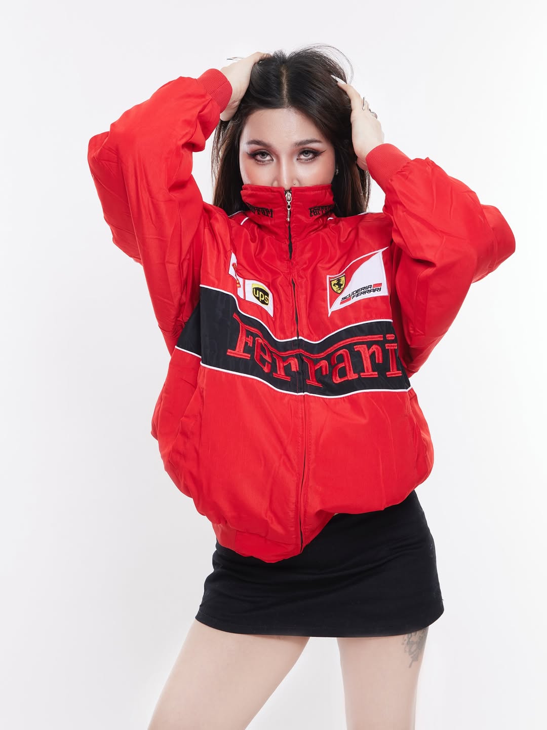 Lifestyle angle of a female model wearing the red Ferrari F1 jacket half-zipped over a white cropped top