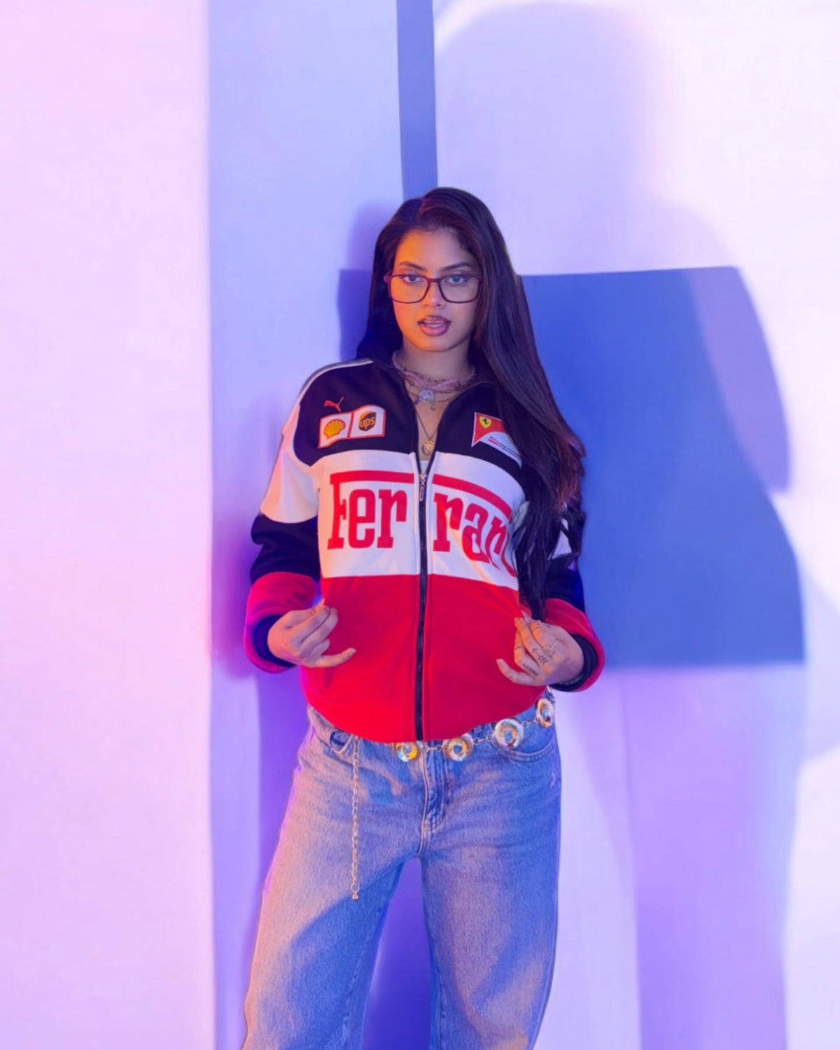 Lifestyle angle of a girl wearing the tri-color Ferrari racing bomber half-zipped over a black crop top

  

  